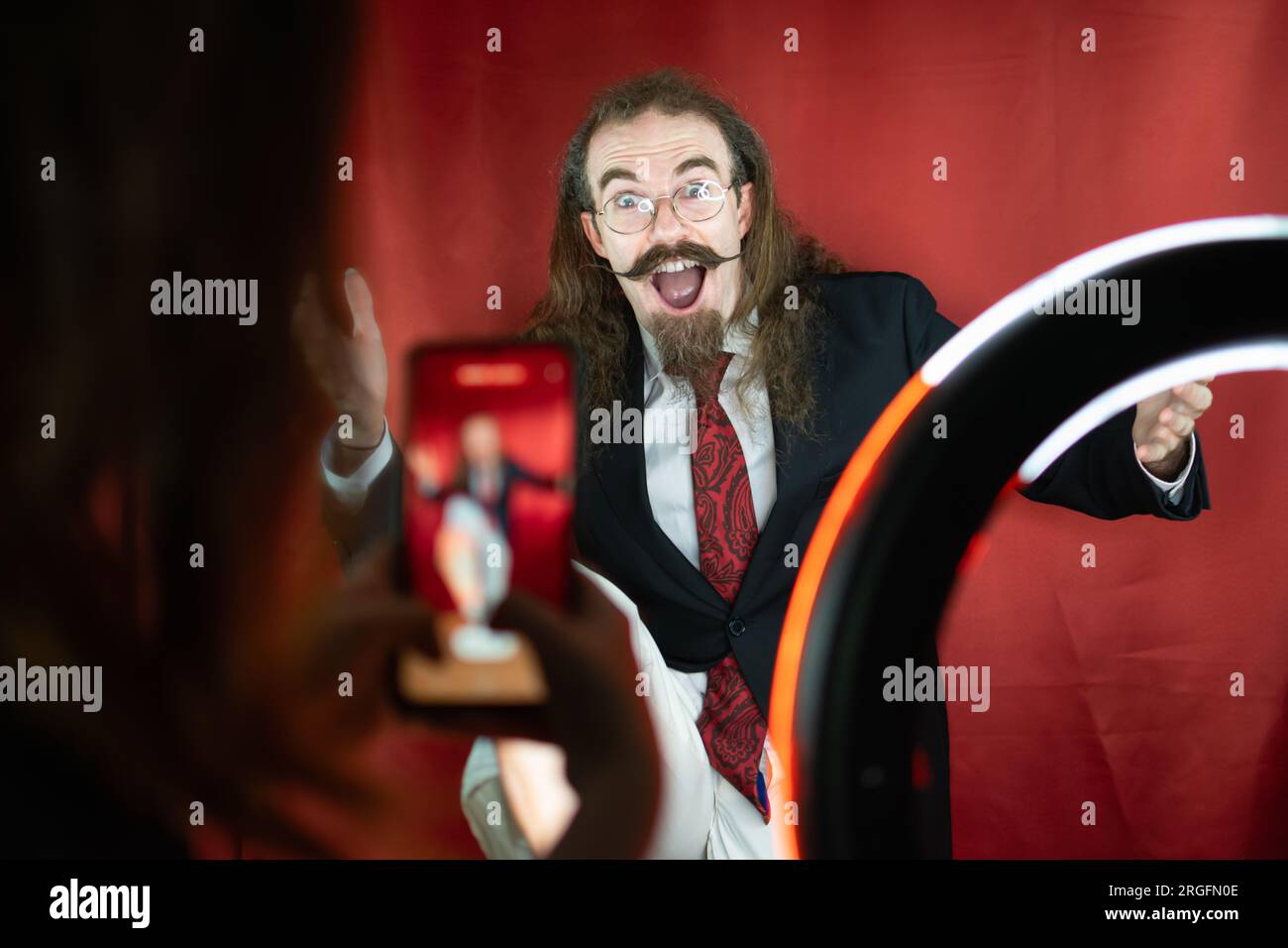 Homme caucasien drôle posant au studio de photographie tout en étant photographié par téléphone portable Banque D'Images
