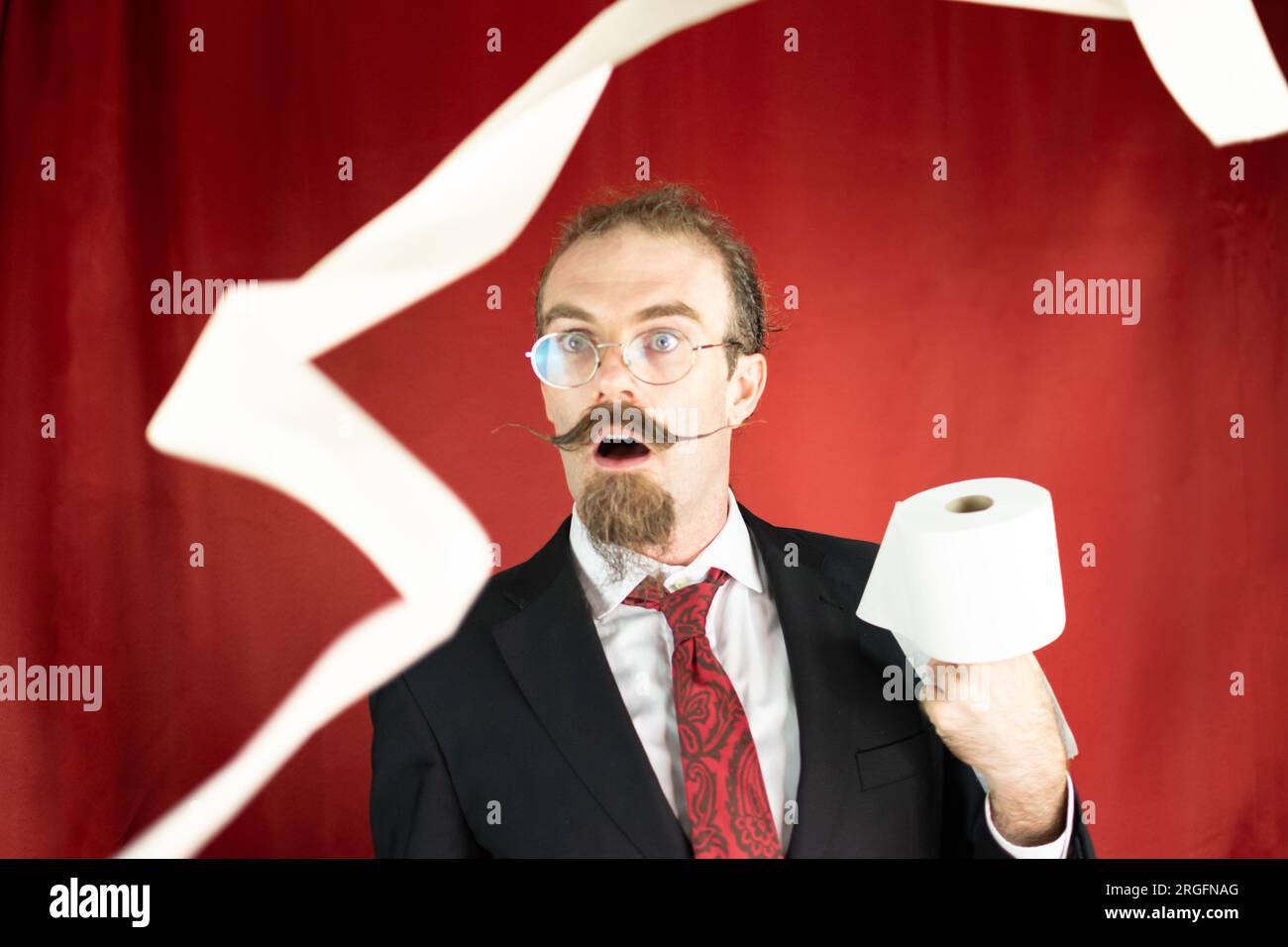 Homme choqué avec des lunettes, cravate rouge et papier toilette à la main regardant comment il vole Banque D'Images