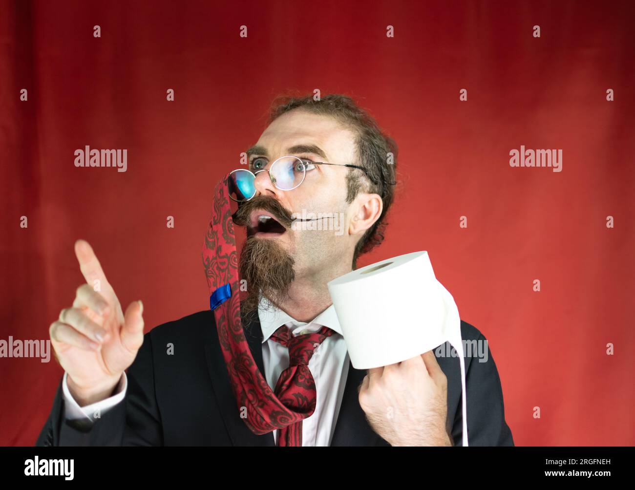 Homme drôle avec des lunettes, cravate rouge sur la tête et papier toilette à la main levant les yeux Banque D'Images