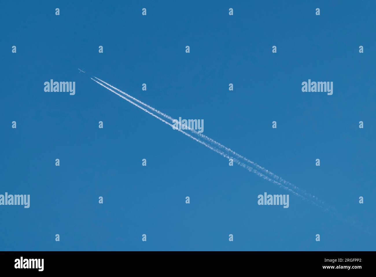 Un avion traverse le ciel bleu en diagonale laissant derrière lui une double traînée blanche Banque D'Images