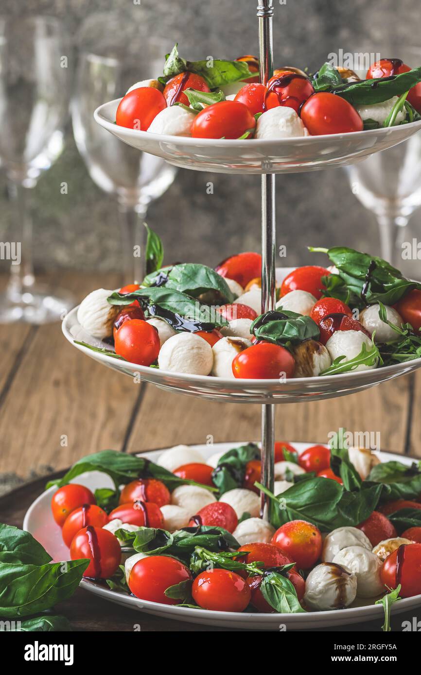 Salade italienne classique Insalata Caprese avec tomates cerises, mini perles de mozarella, feuilles de basilic et glaçage balsamique servi sur un support à gâteaux, vertical Banque D'Images