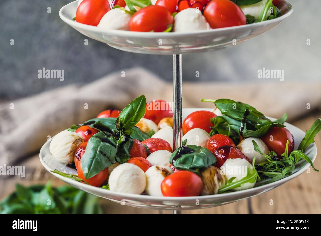 Salade italienne classique Insalata Caprese avec tomates cerises, mini perles de mozarella, feuilles de basilic et glaçage balsamique servi sur un support à gâteaux, en gros plan Banque D'Images
