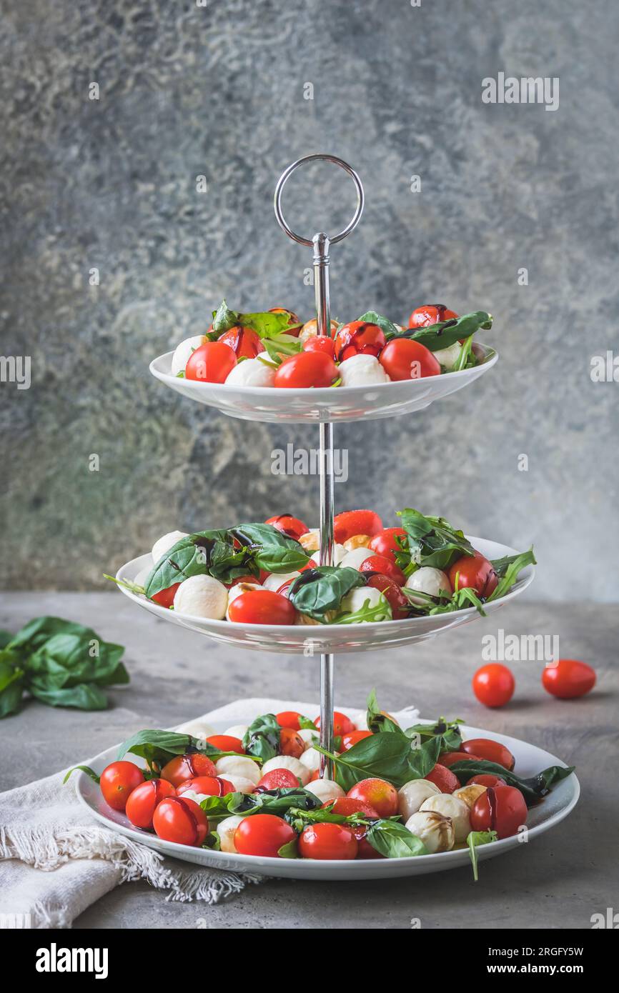 Salade italienne classique Insalata Caprese avec tomates cerises, mini perles de mozarella, feuilles de basilic et glaçage balsamique servi sur un support à gâteaux, vertical Banque D'Images