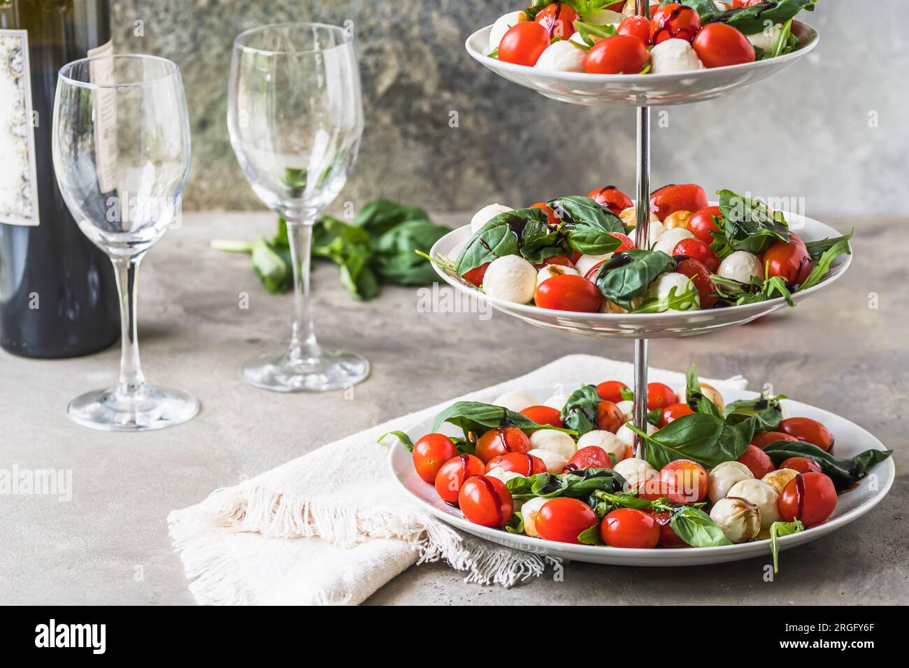 Salade italienne classique Insalata Caprese avec tomates cerises, mini perles de mozarella, feuilles de basilic et glaçage balsamique servi sur un support à gâteau, dos gris Banque D'Images