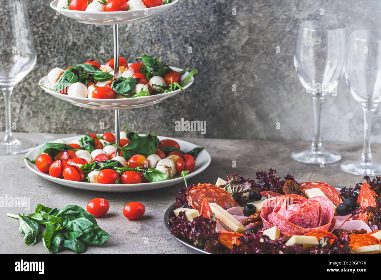 Salade italienne classique Insalata Caprese et une assiette avec une sélection de spécialités de saucisses sur fond gris Banque D'Images