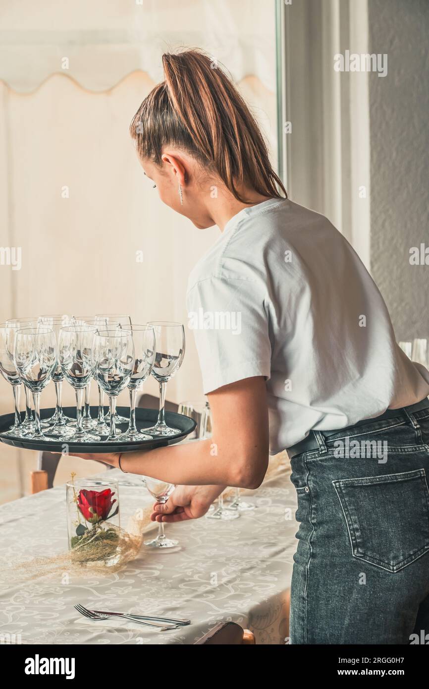 La jeune serveuse met les tables dans le restaurant avec des verres, à la verticale Banque D'Images La jeune serveuse met les tables dans le restaurant avec des verres, à la verticale Banque D'Images