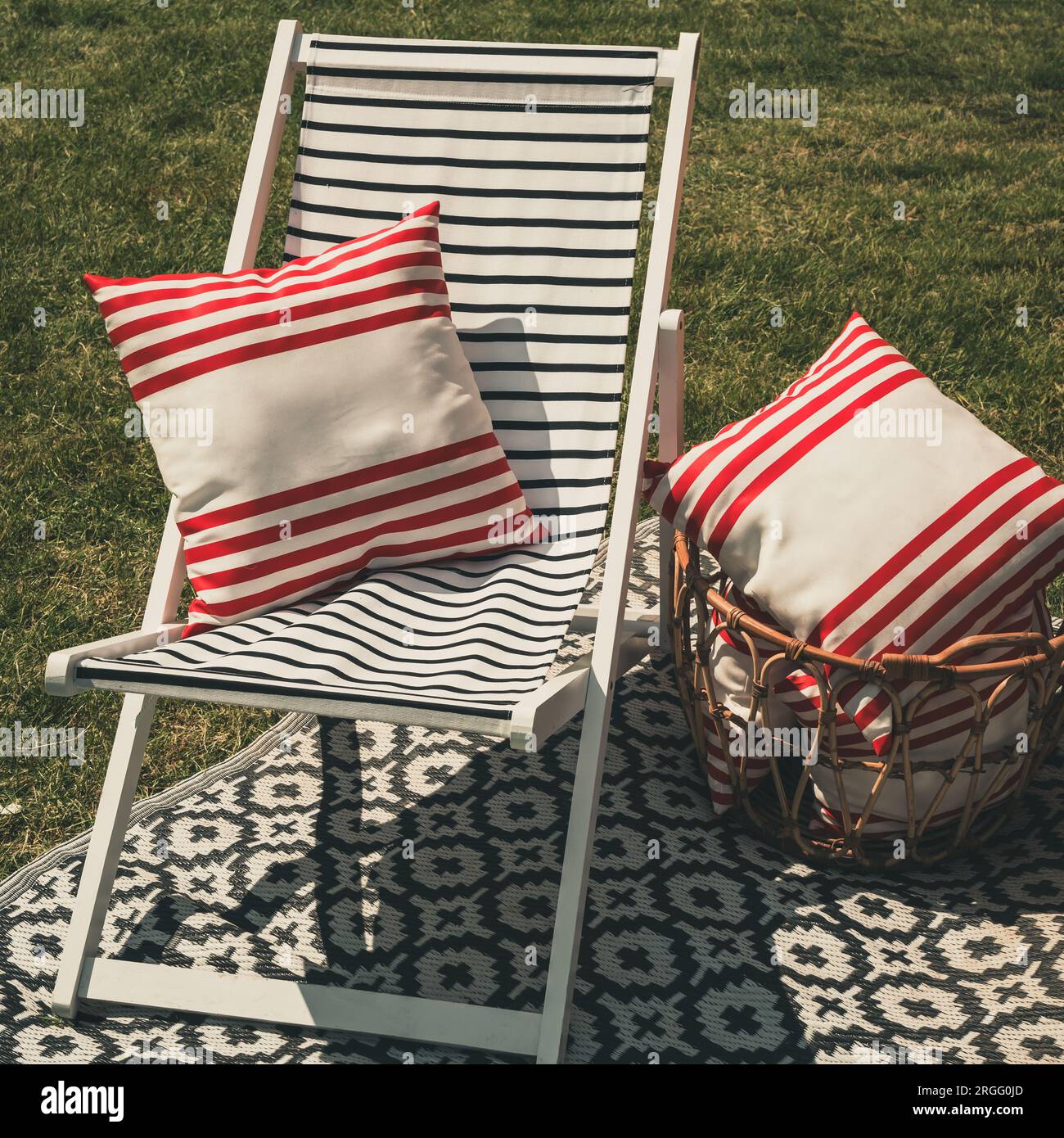 Chaise de jardin confortable avec coussins rouges et blancs sur tapis d'extérieur moderne Banque D'Images