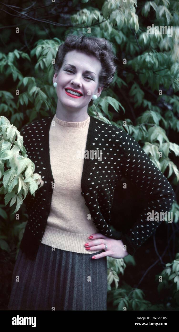 Années 1950, historique, debout à l'extérieur, une dame élégante et attrayante portant une veste à pois sur un pull en laine beige et une jupe crayon de couleur grise, des vêtements qui reflètent ses traits féminins, délicats et raffinés, style sophistiqué, Angleterre, Royaume-Uni. Banque D'Images