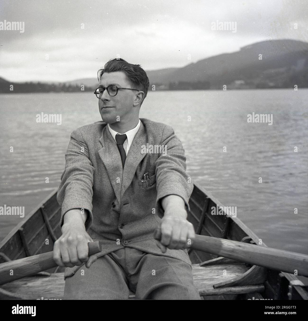 Années 1950, historique, un jeune homme portant une veste de sport, chemise et cravate, ramant un bateau sur un lac, Angleterre, Royaume-Uni. Banque D'Images