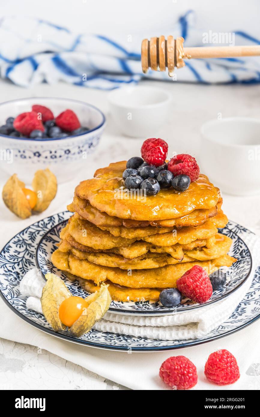Pile de crêpes végétaliennes avec baies et sirop sur un plaque à motifs bleu-blanc sur fond blanc Banque D'Images