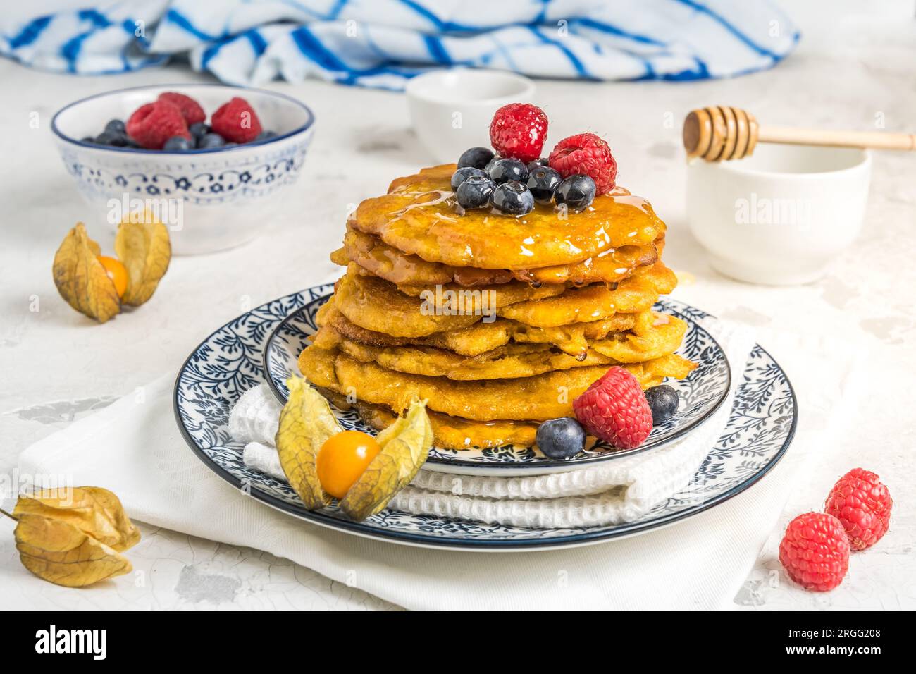 Pile de crêpes végétaliennes avec baies et sirop sur un plaque à motifs bleu-blanc sur fond blanc Banque D'Images