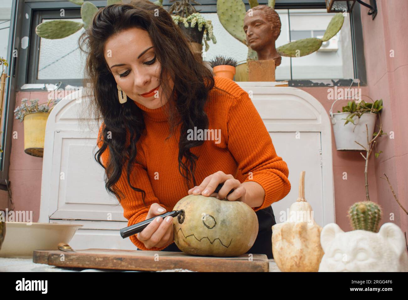 femme caucasienne adulte en chandail orange, debout à la maison avec marqueur peinture citrouille pour halloween night, créant du contenu pour ses réseaux sociaux. Banque D'Images