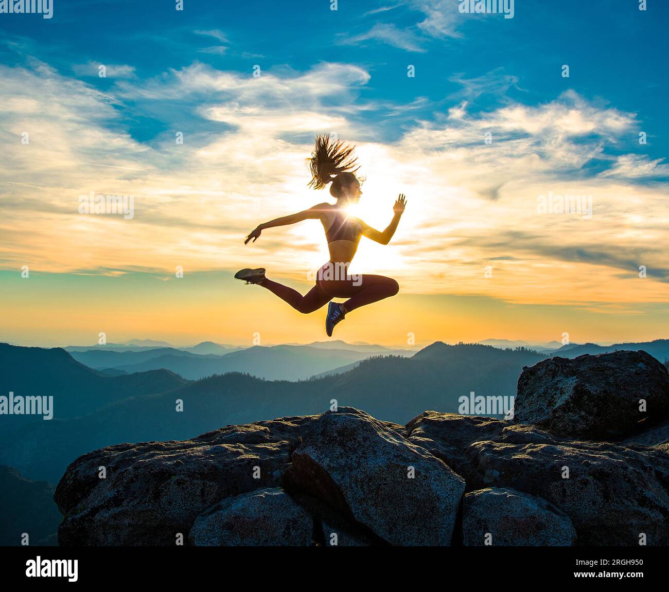 Jeune femme sautant sur une montagne au coucher du soleil Banque D'Images