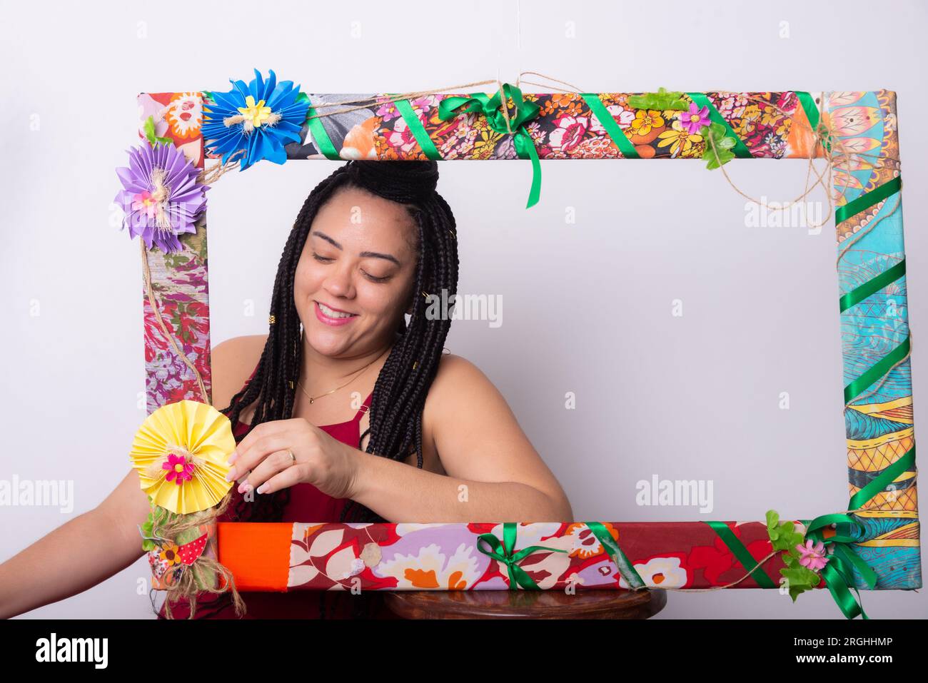 Photo de belle femme avec des tresses dans les cheveux derrière un cadre décoré de fleurs et de tissus colorés dans une position horizontale touchant la fleur Banque D'Images