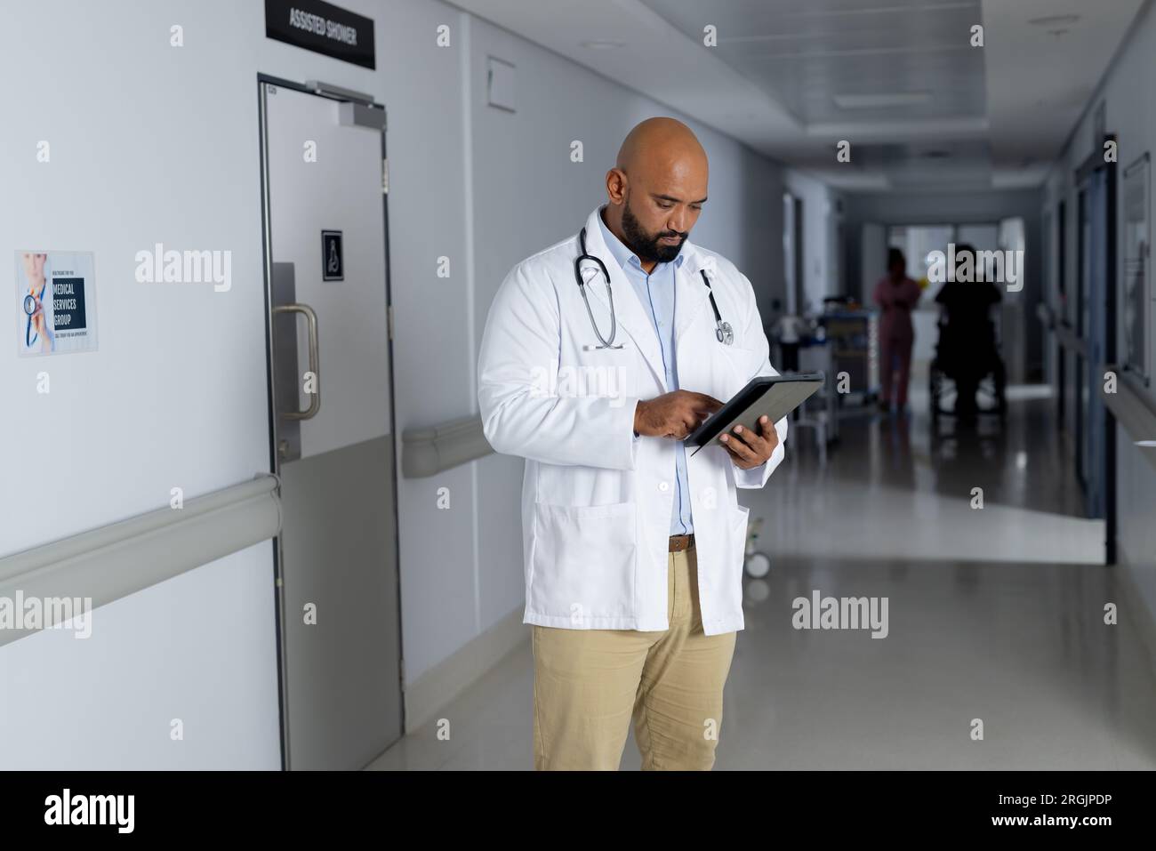 Biracial homme médecin portant une blouse de laboratoire utilisant un comprimé dans le couloir de l'hôpital Banque D'Images