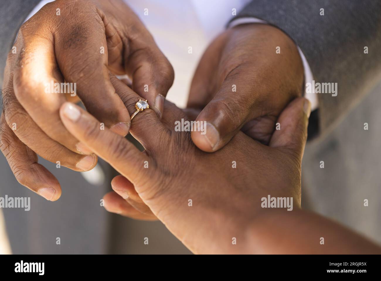 Mains du marié biracial senior mettant la bague de mariage sur le doigt de sa mariée Banque D'Images