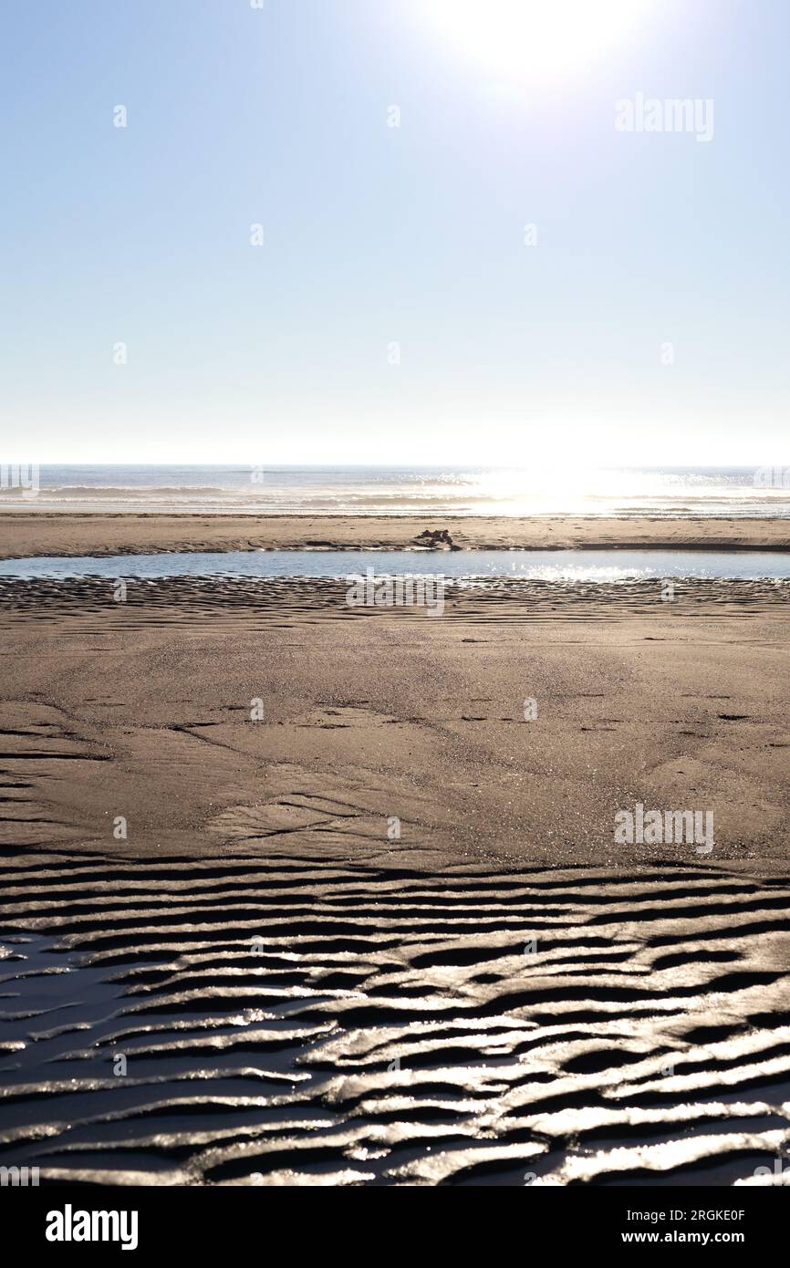 Ondulations dans le sable au premier plan et océan en arrière-plan, sous un ciel ensoleillé. Banque D'Images