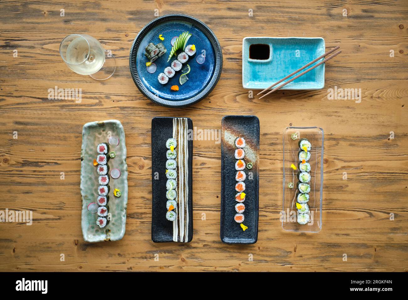 Vue de dessus de sushi assortis et rouleaux sur différentes assiettes en marbre placées sur une table en bois avec des baguettes et un verre à vin Banque D'Images