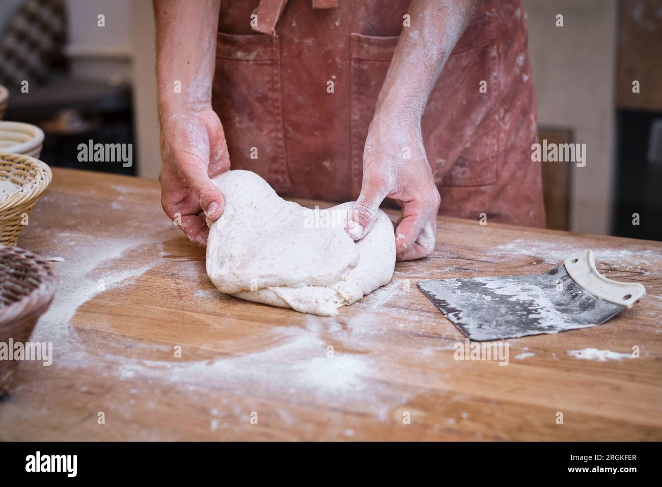Les mains du boulanger mâle travaillent de la pâte à pain avec de la farine sur une table en bois. Banque D'Images