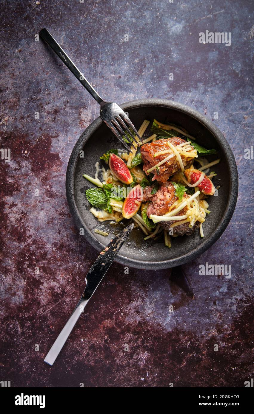 Vue de dessus du trotteur de cochon appétissant avec des figues et des  légumes avec de la verdure sur une plaque noire placée près du couteau et  de la fourchette Photo Stock -