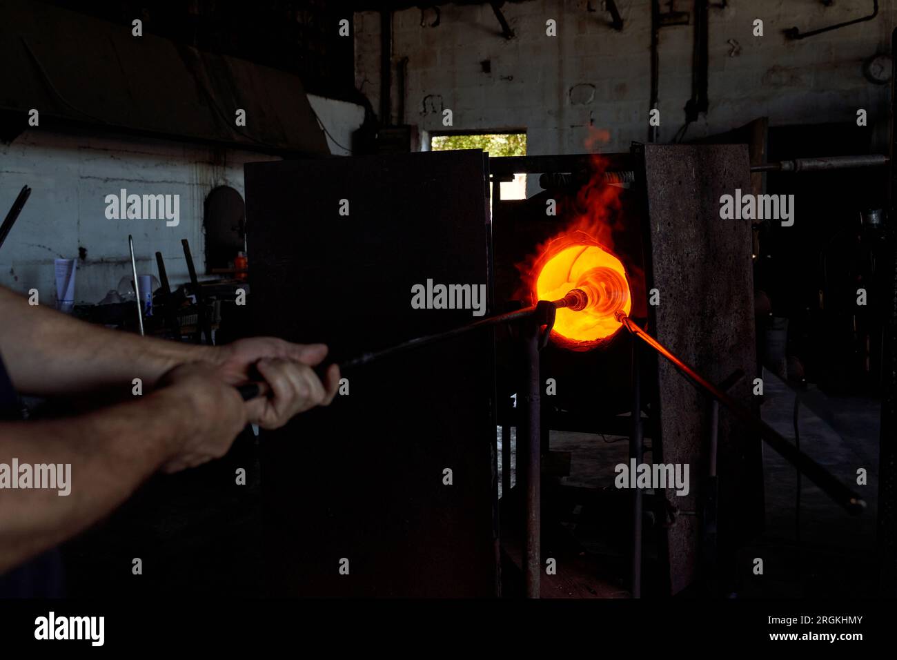 Verrerie masculine méconnaissable mettant la pipe de soufflage en métal avec le verre chauffé sous forme de vase narguilé sur la pointe dans le four de recuit tout en travaillant à l'usine Banque D'Images