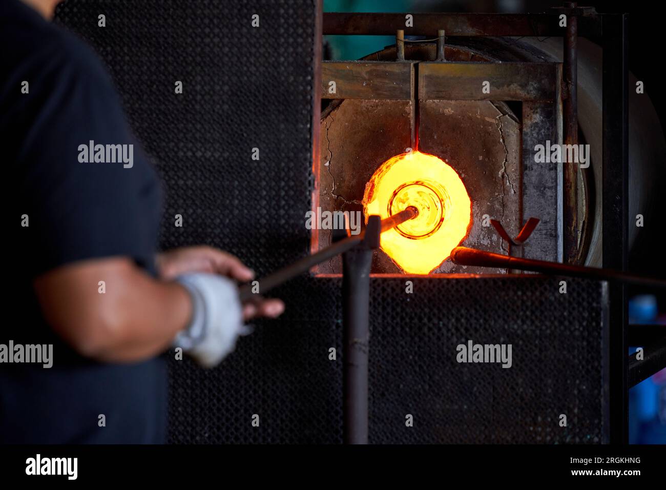 Cultivez le travailleur masculin anonyme mettant la tige de fer avec l'objet en verre attaché dans le four à l'usine pendant le processus de production Banque D'Images