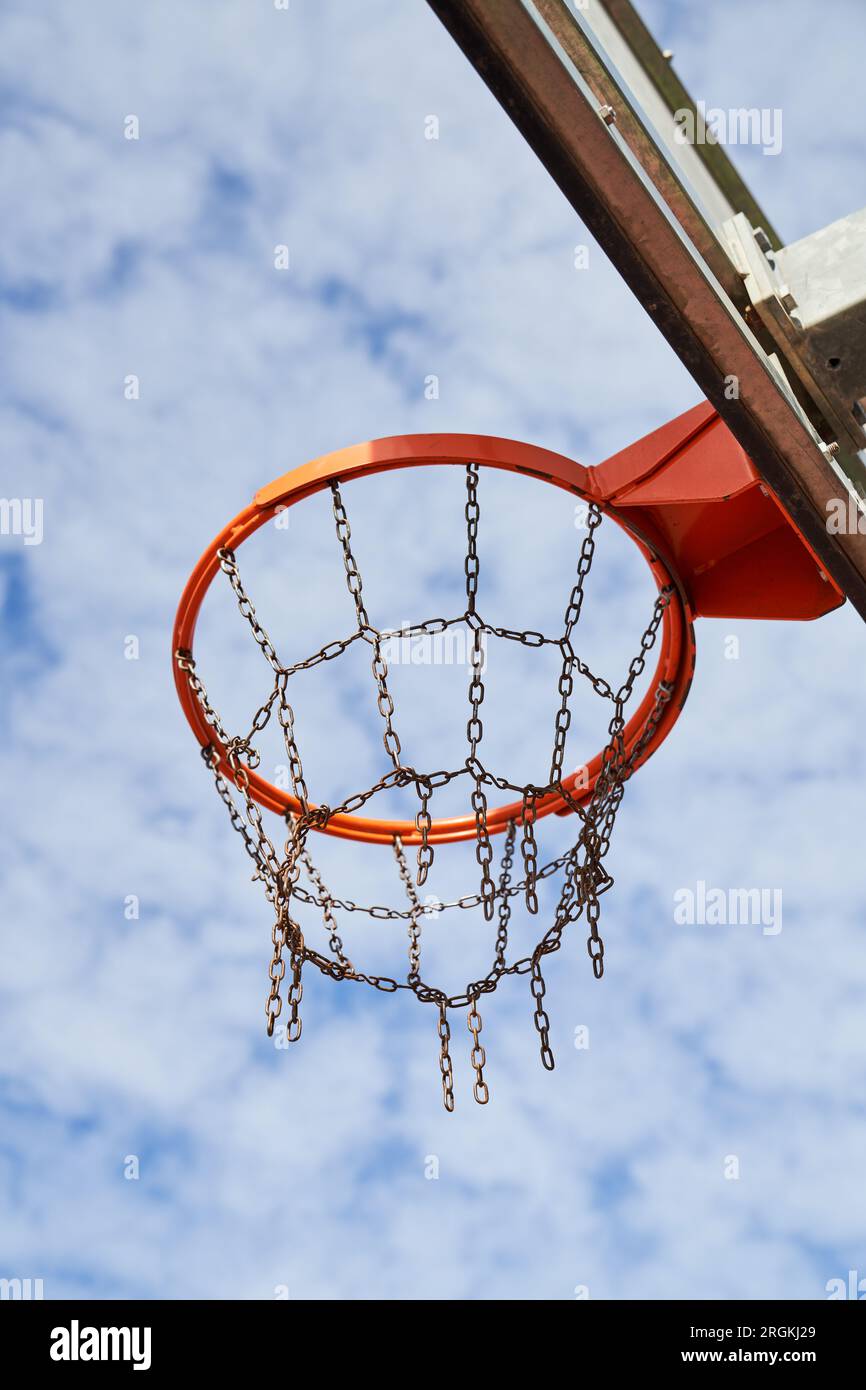 Angle bas de la jante de basket avec filet de chaîne placé sur le panneau arrière sur fond de ciel bleu nuageux Banque D'Images
