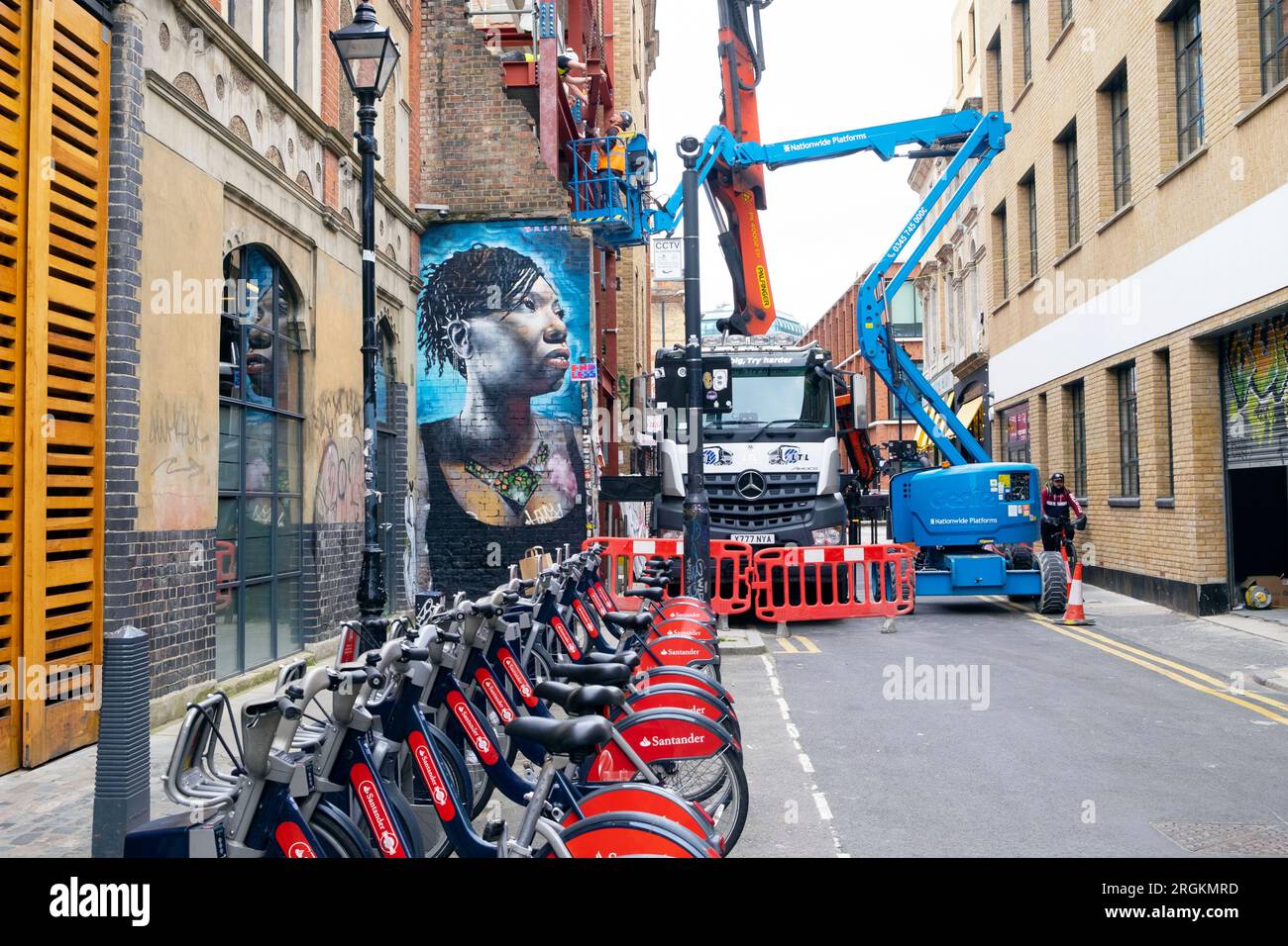 Route fermée bloquée par camion de construction avec grue et cerise picker véhicules murale femme noire Spitalfields East London E1 Angleterre KATHY DEWITT Banque D'Images