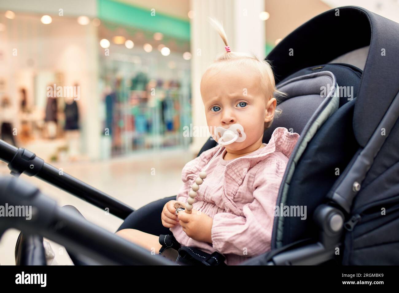Portrait rapproché d'un petit enfant dans une voiture, petite fille blonde dans des vêtements roses avec sucette de bébé. Maman avec un bébé dans une poussette marchant autour de TH Banque D'Images