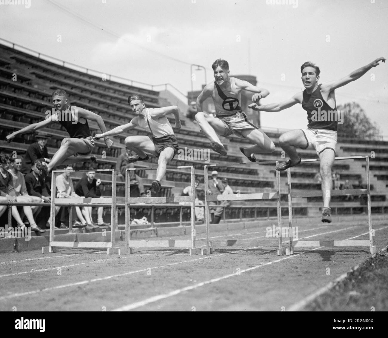 Athlètes d'athlétisme sautant des obstacles pendant un relais à une compétition d'athlétisme d'école secondaire ca. 1924 Banque D'Images