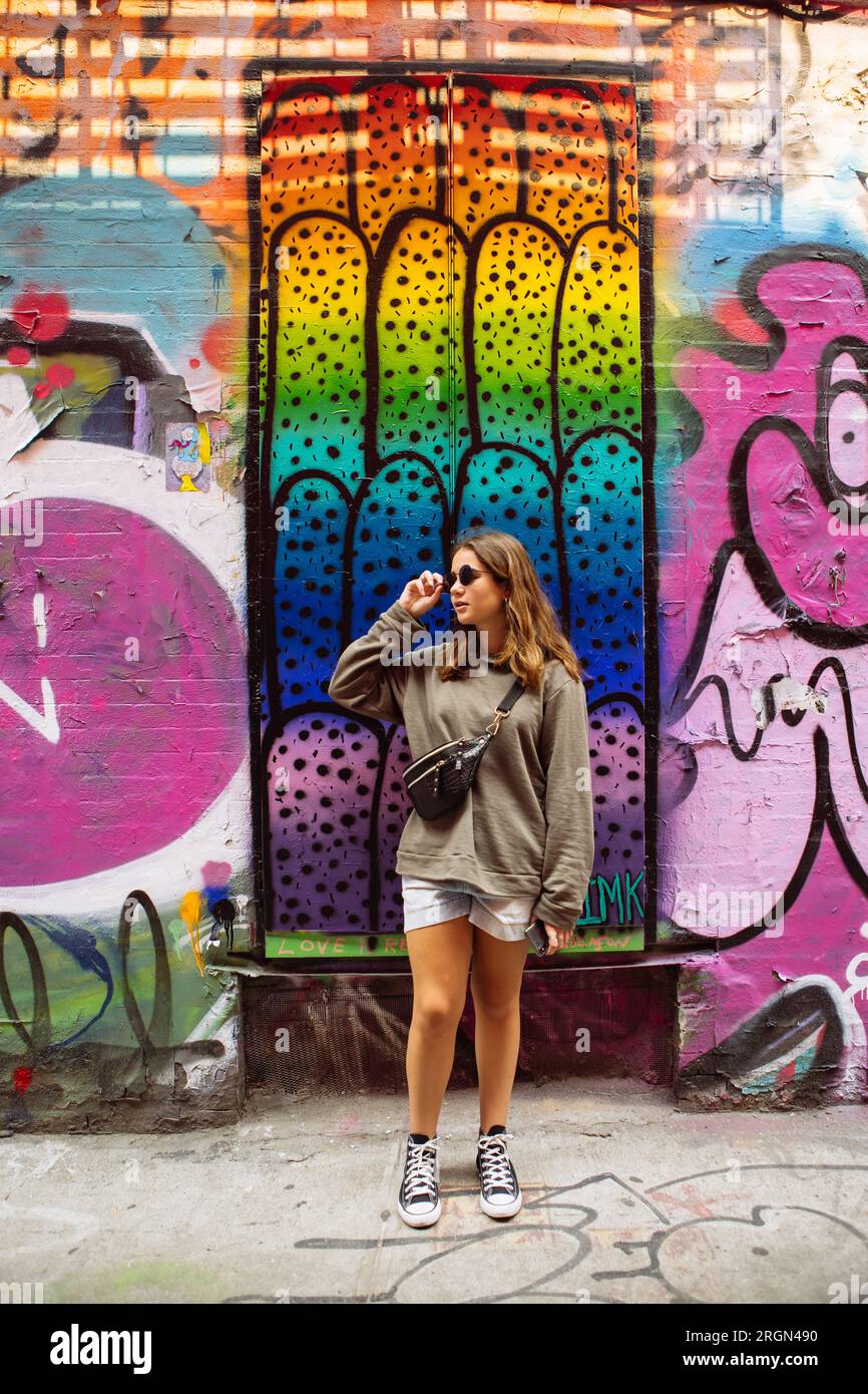 Adolescente posant dans une pose cool avec des lunettes de soleil avec des murs d'art graffiti dans Freeman Alley à Bowery, Manhattan, New York City, USA Banque D'Images