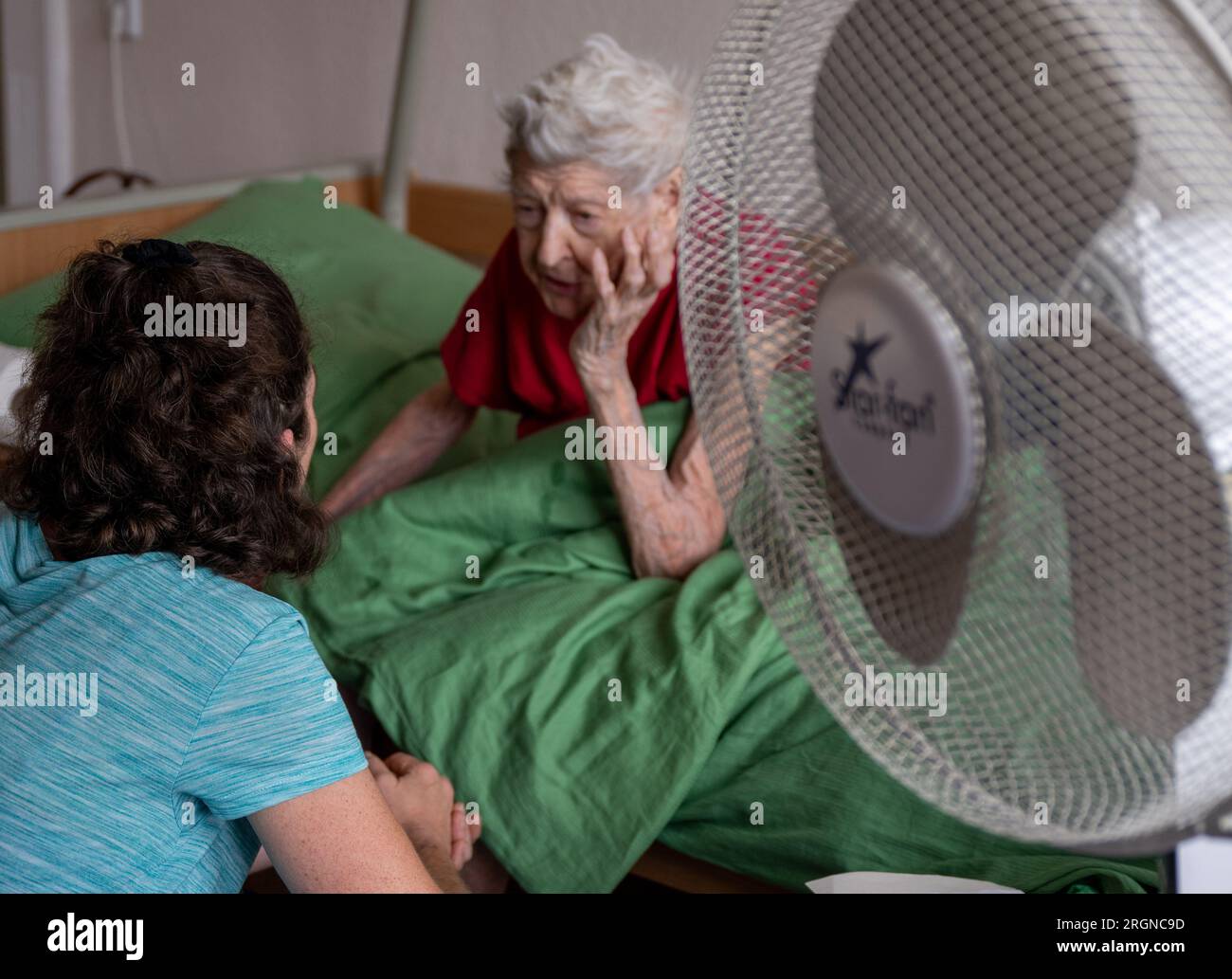 Berlin, Allemagne. 31 juillet 2023. L’infirmière Ramona Rössner parle à sa patiente, Brigitte Richter, âgée de 97 ans, qui a besoin de soins, lors d’une visite à domicile. Un ventilateur de stand est dans la pièce pour le refroidir dans la chaleur. Crédit : Monika Skolimowska/dpa/Alamy Live News Banque D'Images