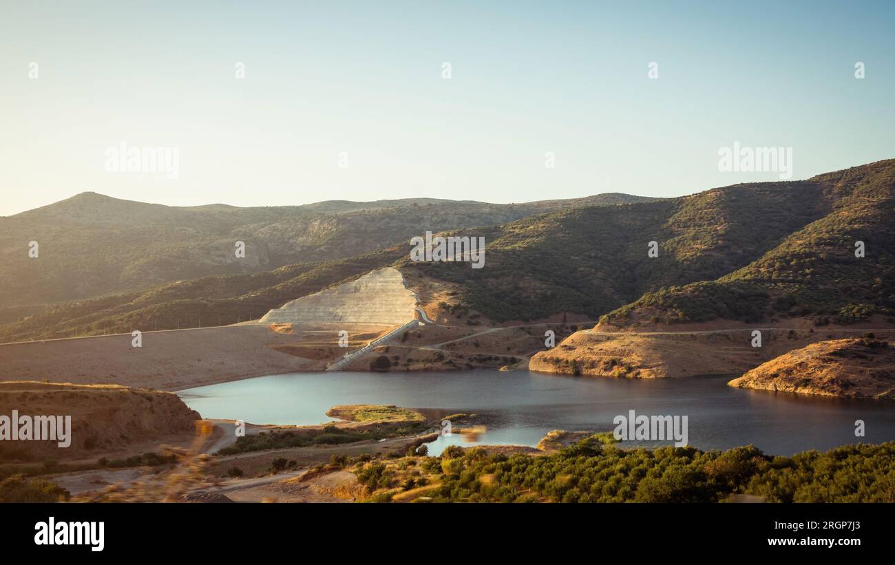 Lac Aposelemis en Crète dans les rayons du soleil couchant. Lac artificiel de montagne au coucher du soleil. Barrage de remblai en terre dans la campagne montagneuse avec des pentes vertes Banque D'Images
