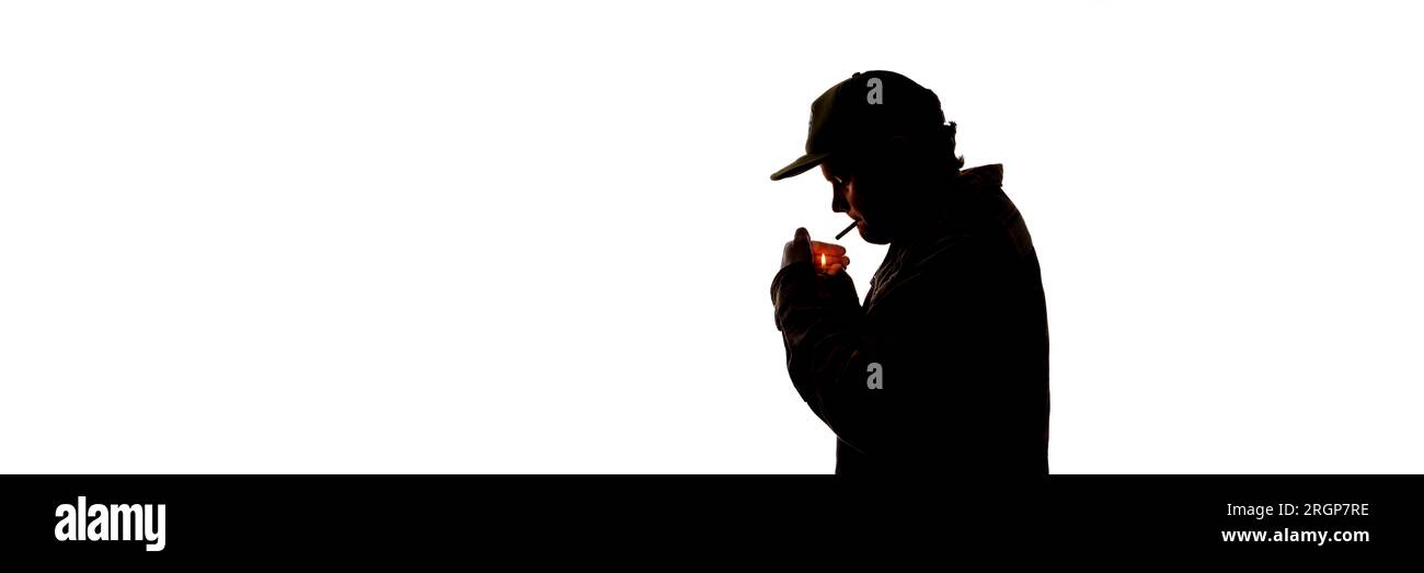 Un jeune homme silhouetté sur blanc allume une cigarette Banque D'Images