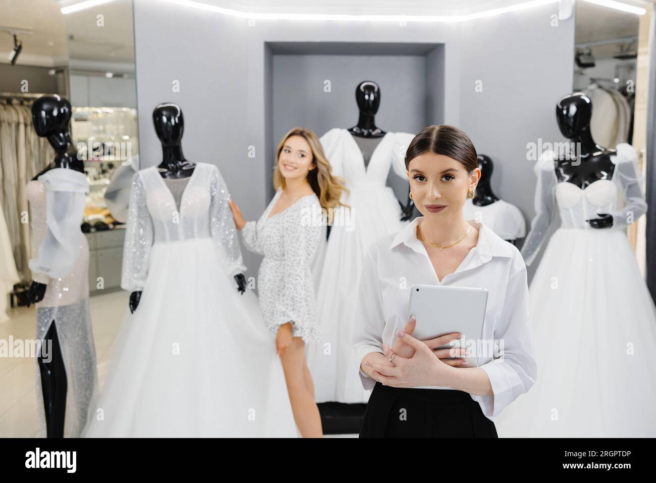 Les femmes propriétaires de magasin de mariée attrayantes utilisent la tablette numérique pour aider le client à choisir la robe de mariée au magasin. Banque D'Images