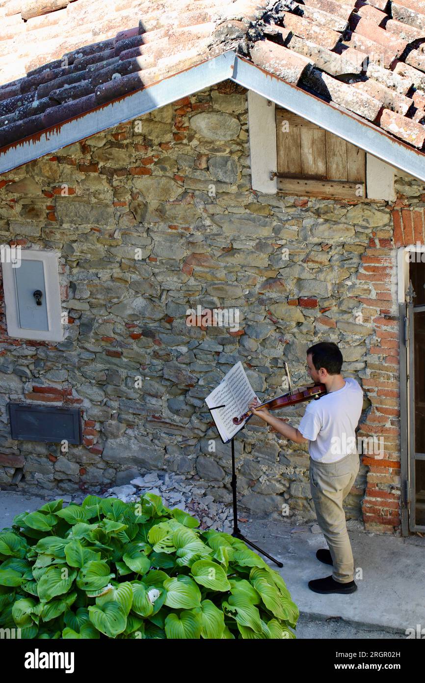 Un violoniste pratique à l'extérieur d'une école de musique dans le petit village italien de sale San Giovanni, Cuneo, Piémont, Italie Banque D'Images