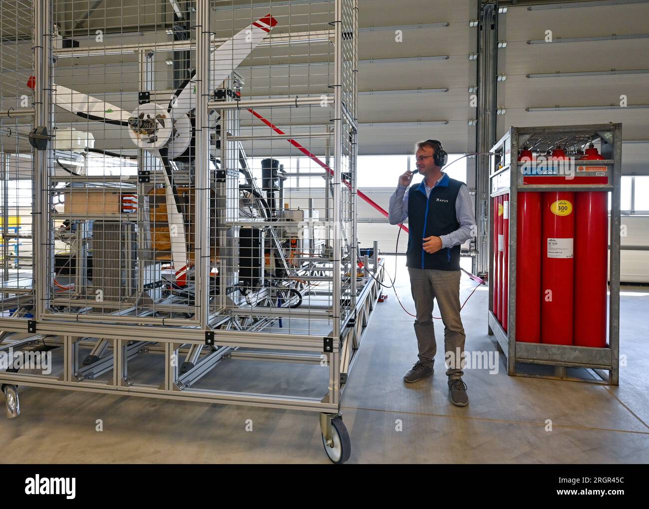 11 août 2023, Brandenburg, Strausberg : Alexander Behrens, ingénieur de développement chez APUS GmbH, se tient à côté d'un moteur d'avion à hydrogène qu'il a développé. APUS GmbH, leader dans le développement et la fabrication d’avions à hydrogène, a ouvert le même jour une usine d’essais et d’assemblage final à Strausberg. L'installation représente un investissement important pour l'avenir de l'aviation et aidera APUS à développer et à tester ses avions fonctionnant à l'hydrogène. Le centre d'essai du complexe est principalement utilisé pour les essais de propulsion. À cette fin, un banc d'essai a été construit pour tester la pile à combustible, les batteries et l'électricité hybride Banque D'Images