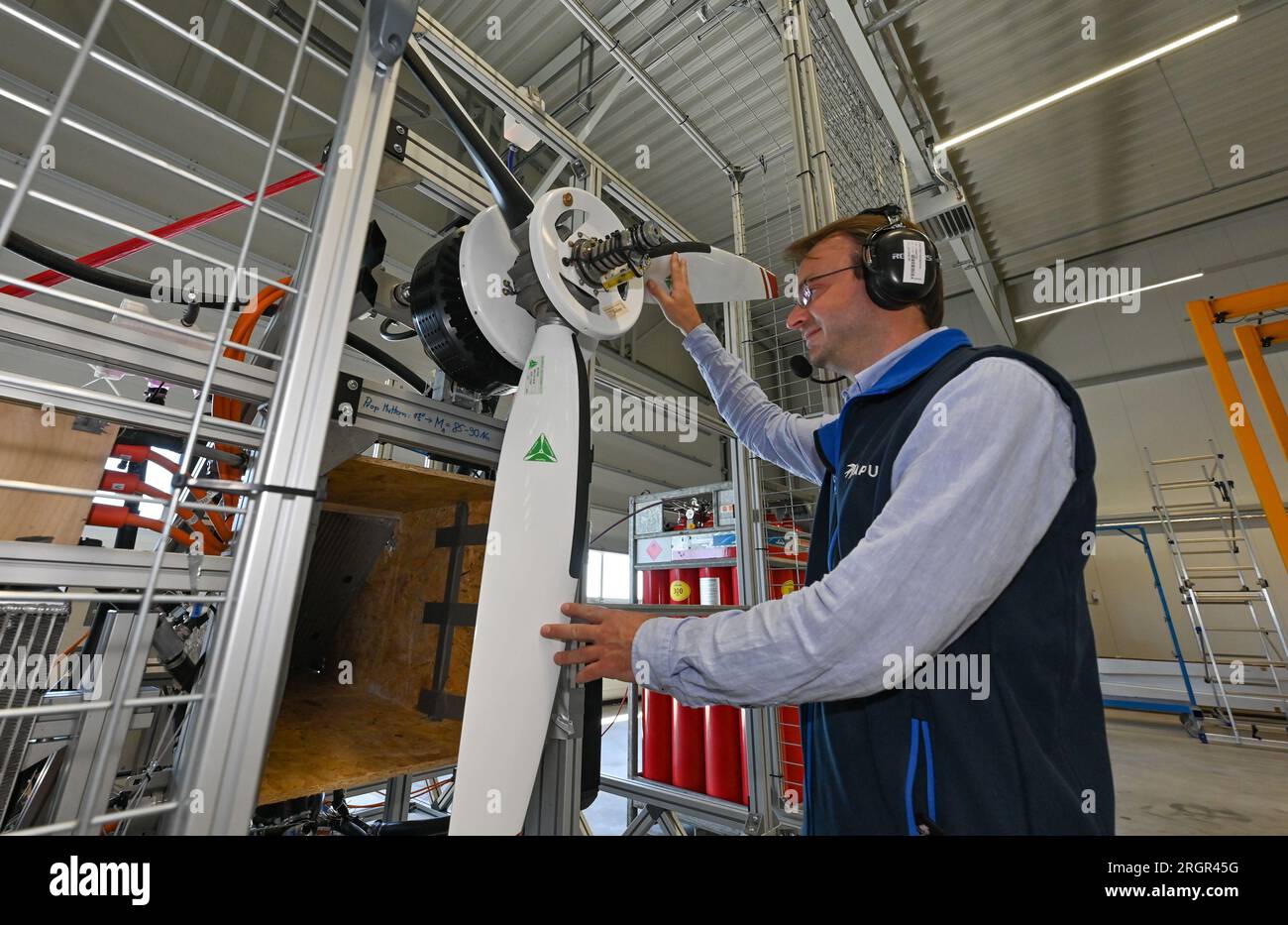 11 août 2023, Brandenburg, Strausberg : Alexander Behrens, ingénieur de développement chez APUS GmbH, se tient devant un moteur d'avion à hydrogène qu'il a développé. APUS GmbH, leader dans le développement et la fabrication d’avions à hydrogène, a ouvert le même jour une usine d’essais et d’assemblage final à Strausberg. L'installation représente un investissement important pour l'avenir de l'aviation et aidera APUS à développer et à tester ses avions fonctionnant à l'hydrogène. Le centre d'essai du complexe est principalement utilisé pour les essais de propulsion. À cette fin, un banc d'essai a été construit pour tester la pile à combustible, les batteries et l'hybride Banque D'Images