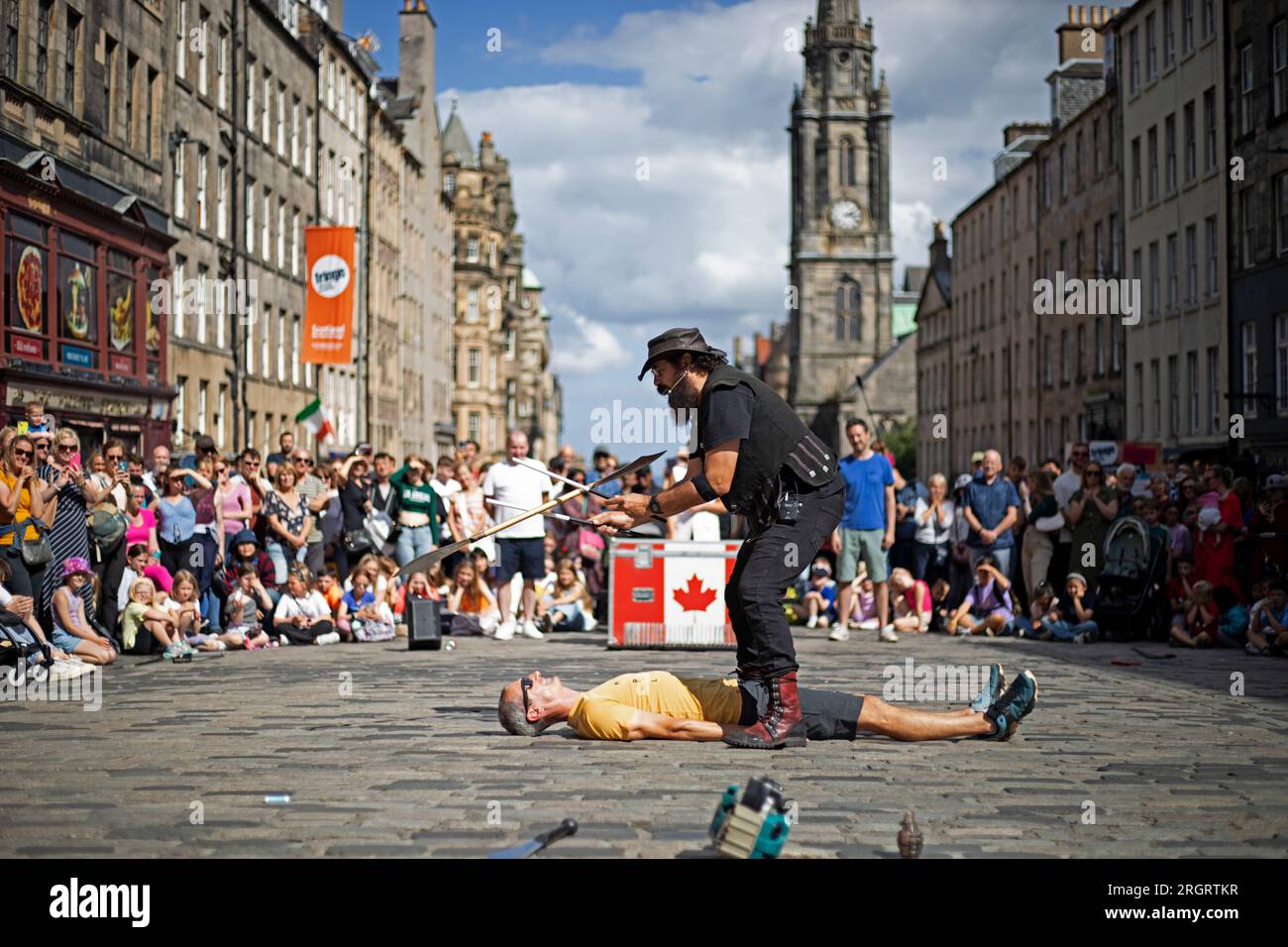 Royal Mile, Écosse, Royaume-Uni. 11 août 2023. Street Performers sur High Street trouver les conditions venteuses difficiles mais le temps chaud bienvenue avec une température un peu plus de 20 degrés. Les foules arrivent plus tard dans la journée avec plusieurs autres emplacements de spectacles autour du centre-ville. Sur la photo : le Stickman jongle un objet pointu semblable à une gâchette au-dessus d'un volontaire du public dans la High Street. Crédit : Archwhite/alamy Live News. Banque D'Images