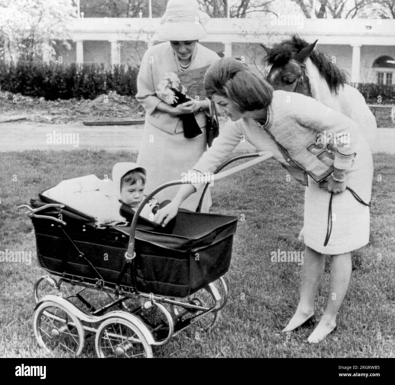 Washington, D.C. : 12 avril 1962 Mme Jacqueline Kennedy présente son fils John à l'impératrice Farah d'Iran alors qu'ils visitent le domaine de la Maison Blanche. Derrière elle se trouve le poney Kennedy, Macaroni. Banque D'Images