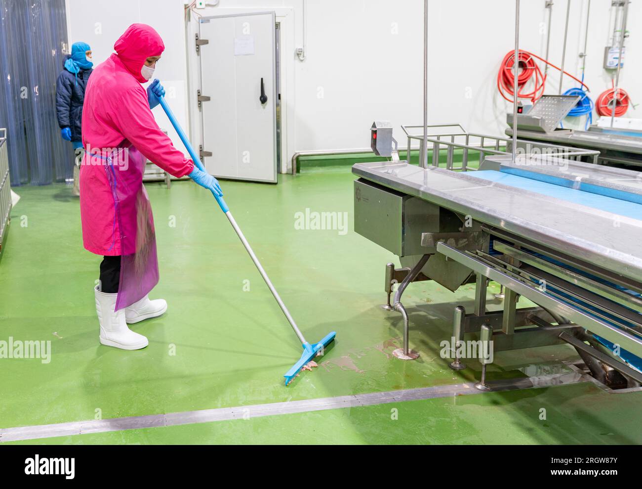 Le travailleur de l'hygiène nettoie le sol après la fin de production du travail dans l'abattoir. Banque D'Images