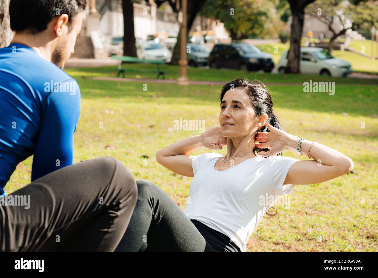 Portrait d'une femme d'âge moyen faisant des exercices abdominaux dans un parc avec son entraîneur personnel. Concept de sport de plein air Banque D'Images