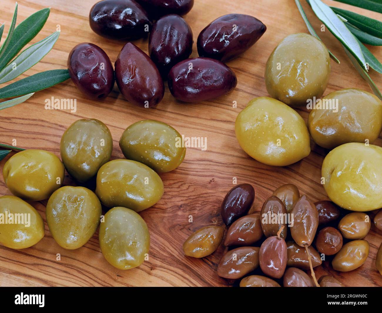 Gros plan de différents types d'olives sur une assiette de service en bois, des olives mélangées de différentes tailles comme un apéritif sain Banque D'Images