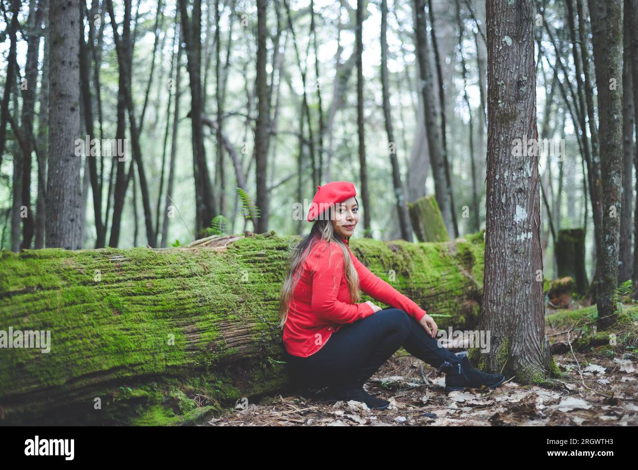 Femme souriante couchée sur un tronc d'arbre mousseline au milieu de la forêt regardant la caméra. Banque D'Images