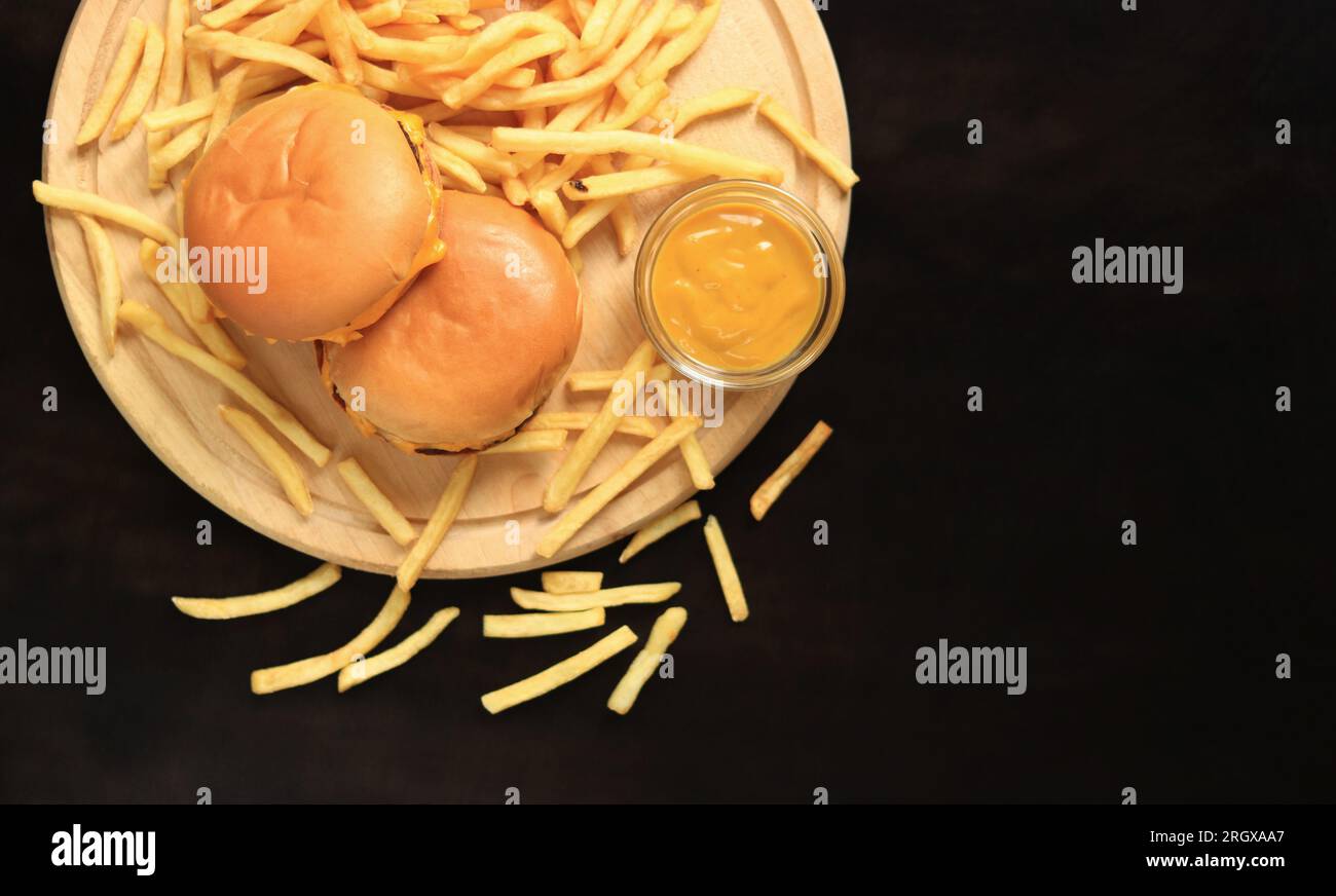 Cheeseburgers et frites sur une planche à découper, vue de dessus, fond en bois foncé. Restauration rapide. Hamburgers, frites et moutarde Banque D'Images