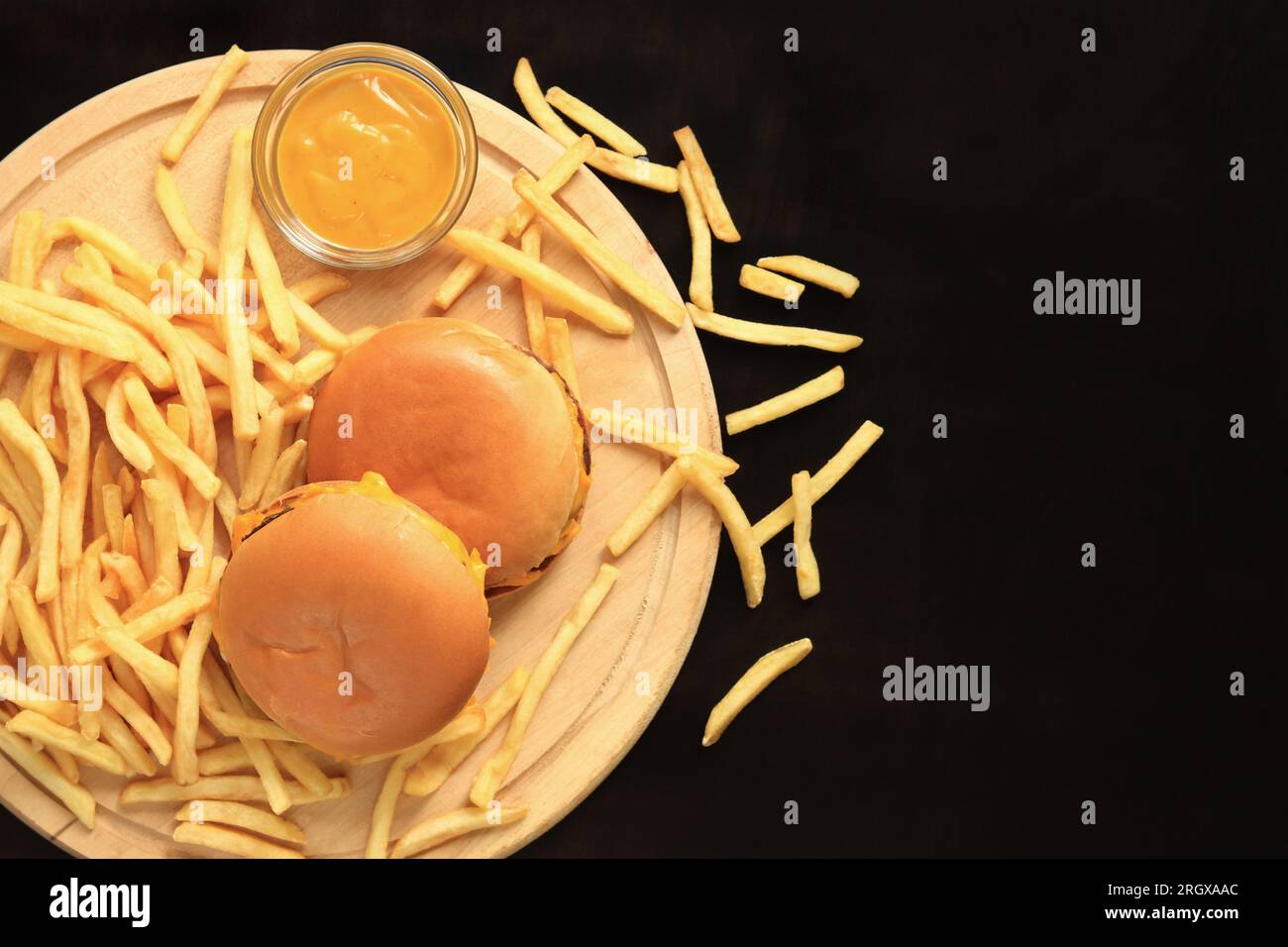 Cheeseburgers et frites sur une planche à découper, vue de dessus, fond en bois foncé. Restauration rapide. Hamburgers, frites et moutarde Banque D'Images