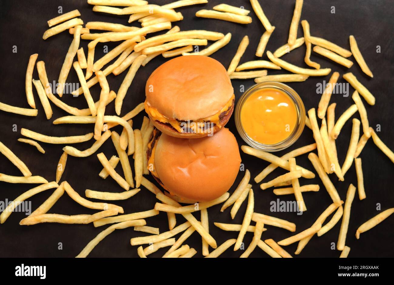 Deux cheeseburgers, frites éparpillées sur une table sombre en bois et moutarde, vue de dessus. Délicieux fast-food. Hamburgers Banque D'Images