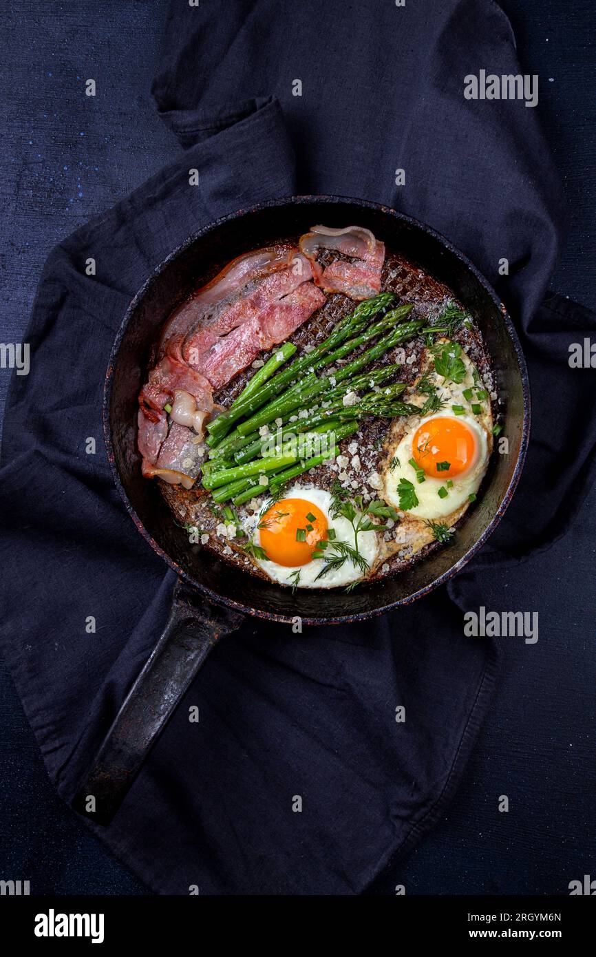 Délicieux petit déjeuner branche de déjeuner avec œufs frits, bacon, asperges vertes, verdure et parmesan sur la poêle. Vue de dessus, espace copie Banque D'Images