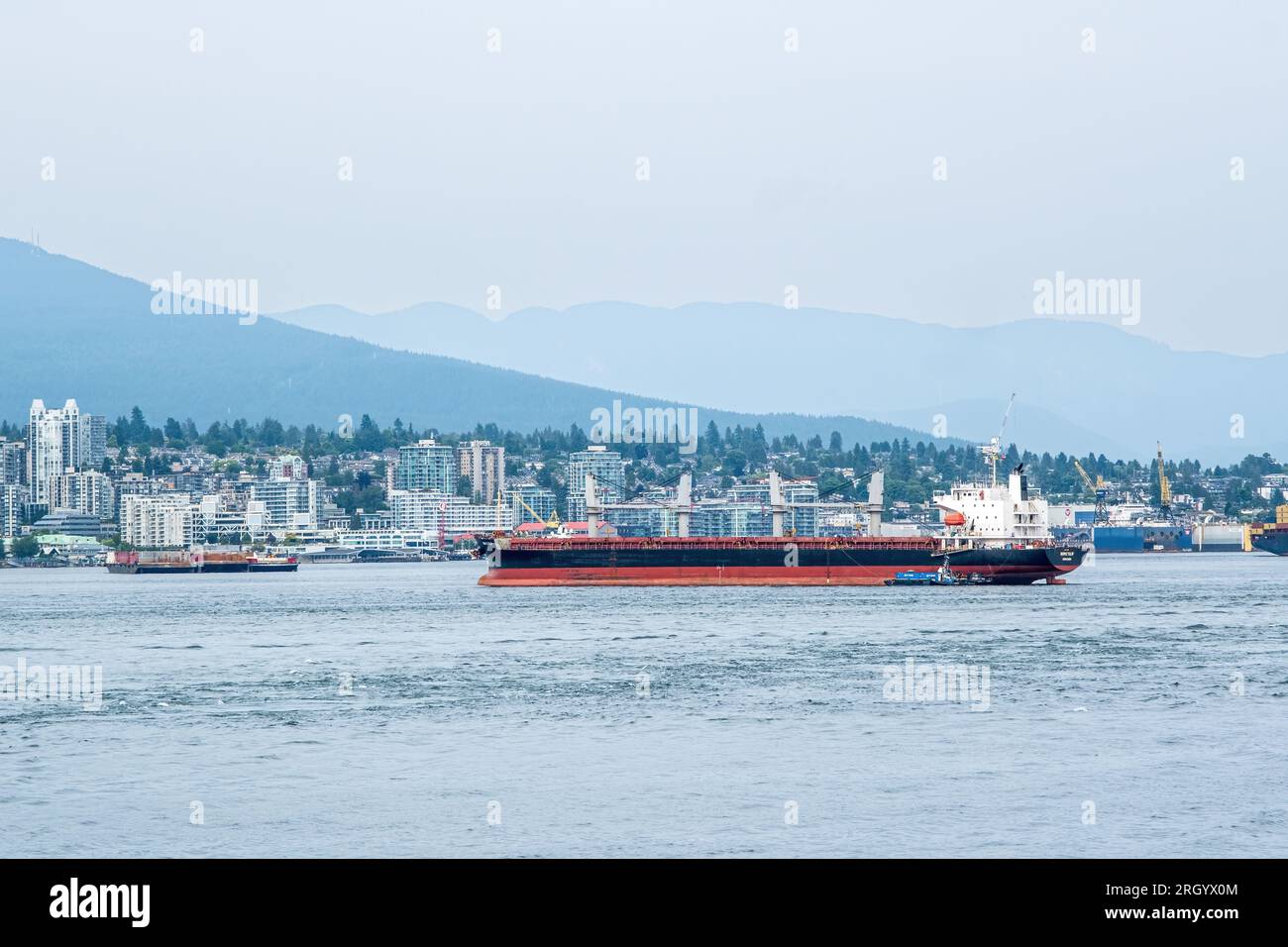 Un grand navire océanographique est guidé dans le port de Vancouver par des remorqueurs. Banque D'Images