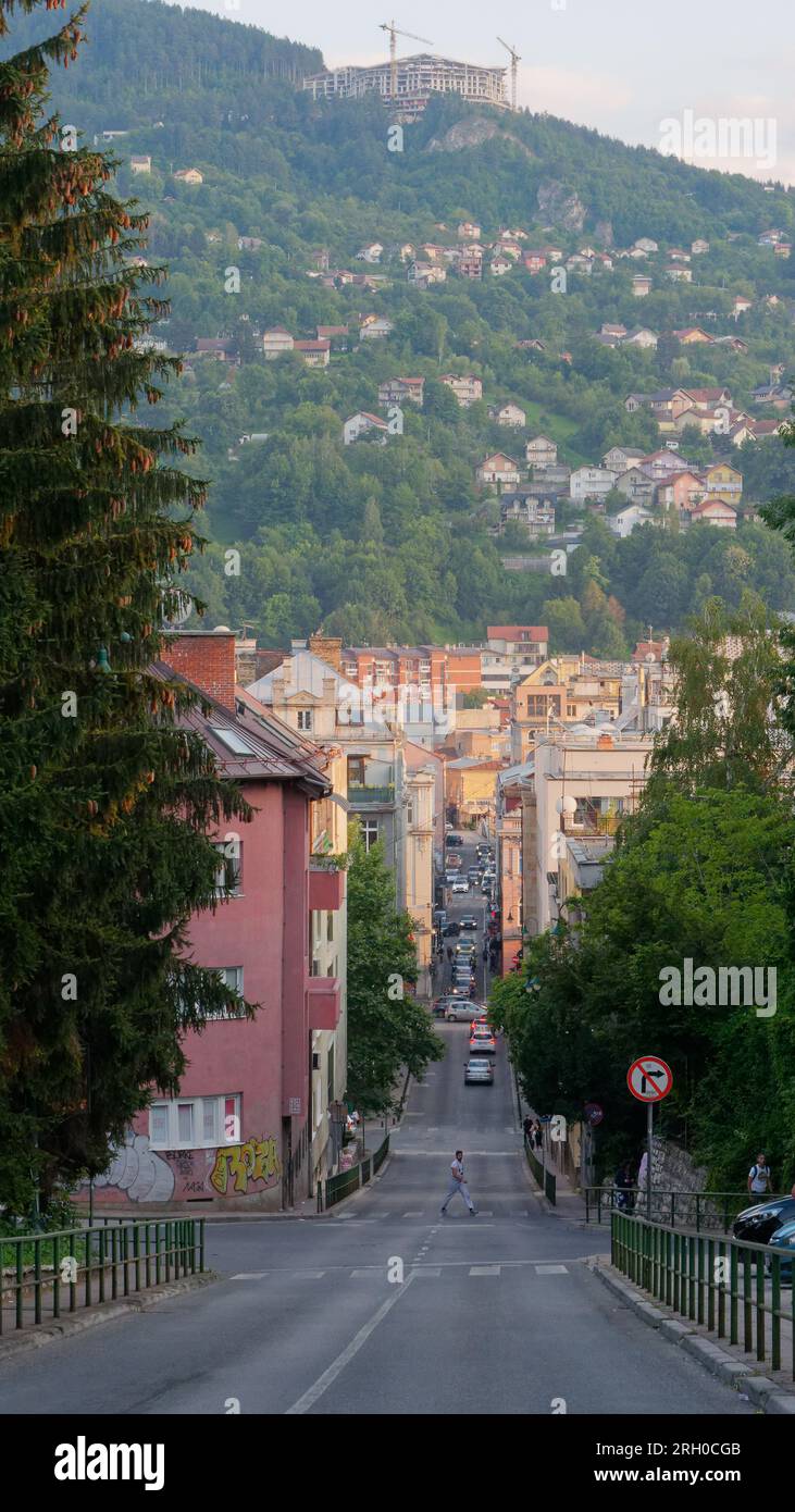 Un homme traverse une rue escarpée avec des montagnes en arrière-plan dans la ville de Sarajevo, le 12 août 2023. Banque D'Images